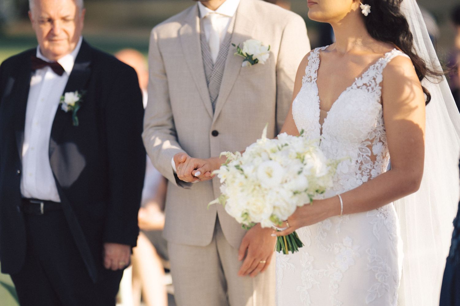 Wedding couple celebrates during a sunny outdoor ceremony while holding elegant white floral bouquets.