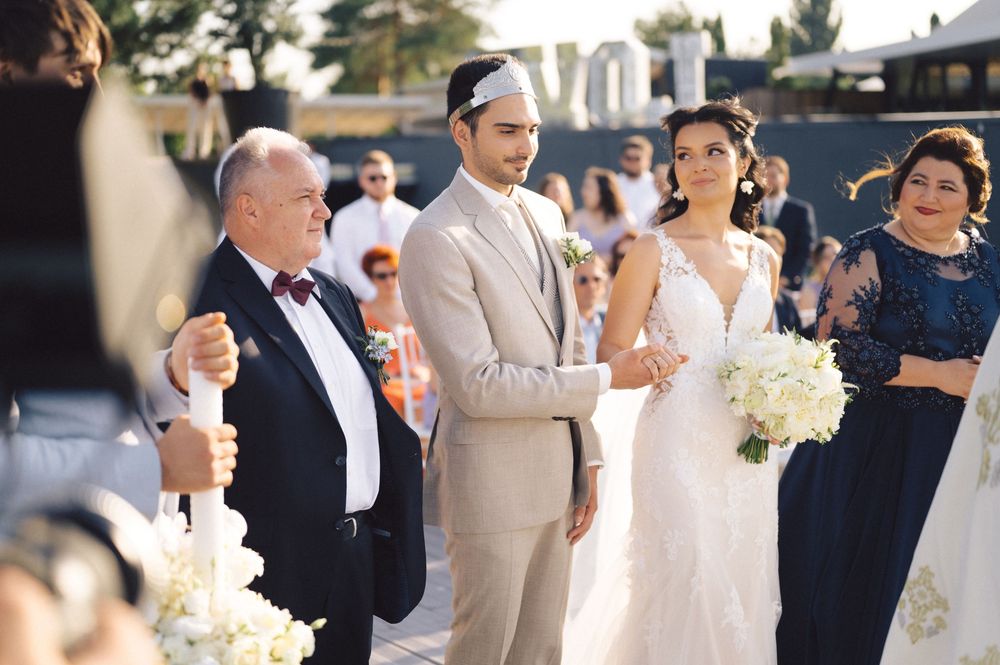 Wedding party members gathered outdoors on a sunny day with the bride holding a white bouquet.