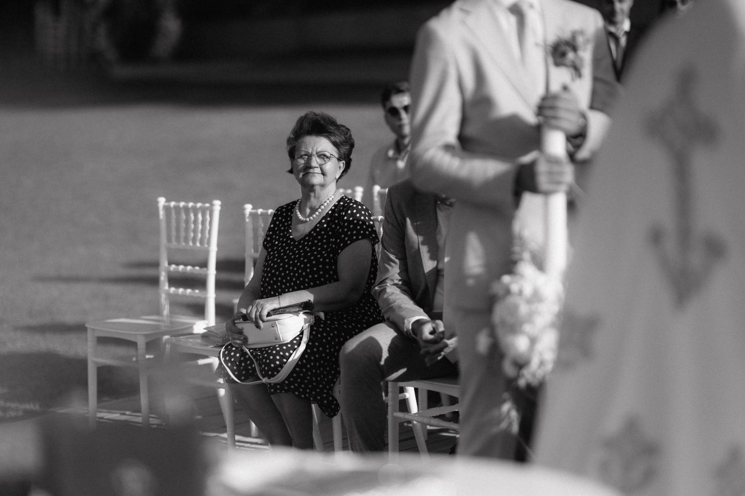 Black and white photograph of someone sitting in a white chair holding a banjo at an outdoor event.