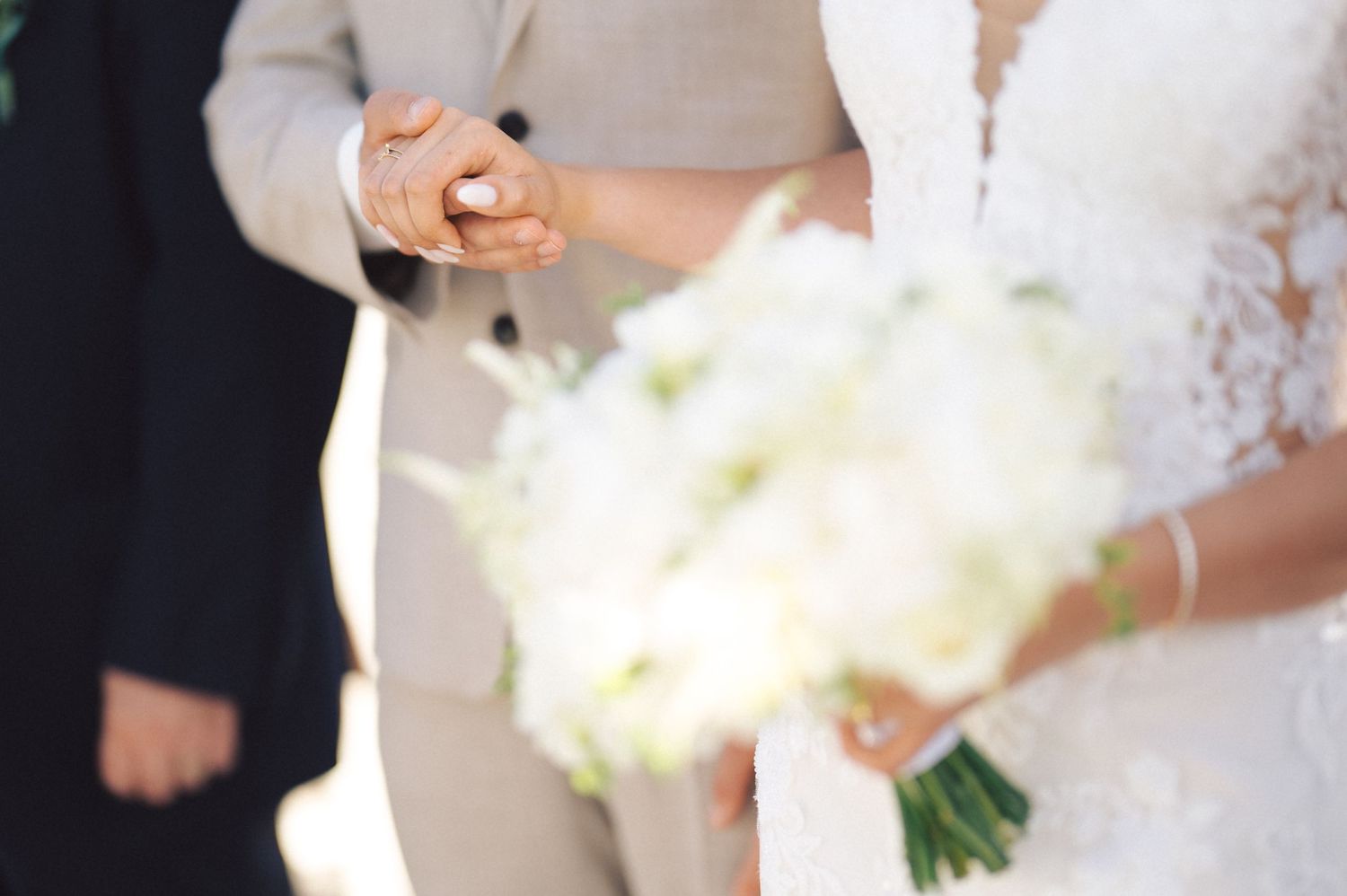 Wedding couple exchanging their rings during ceremony with close-up view of hands and floral bouquet.
