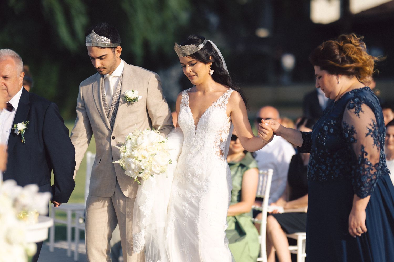 People gather outdoors for an elegant garden wedding ceremony with white floral decorations and arches.