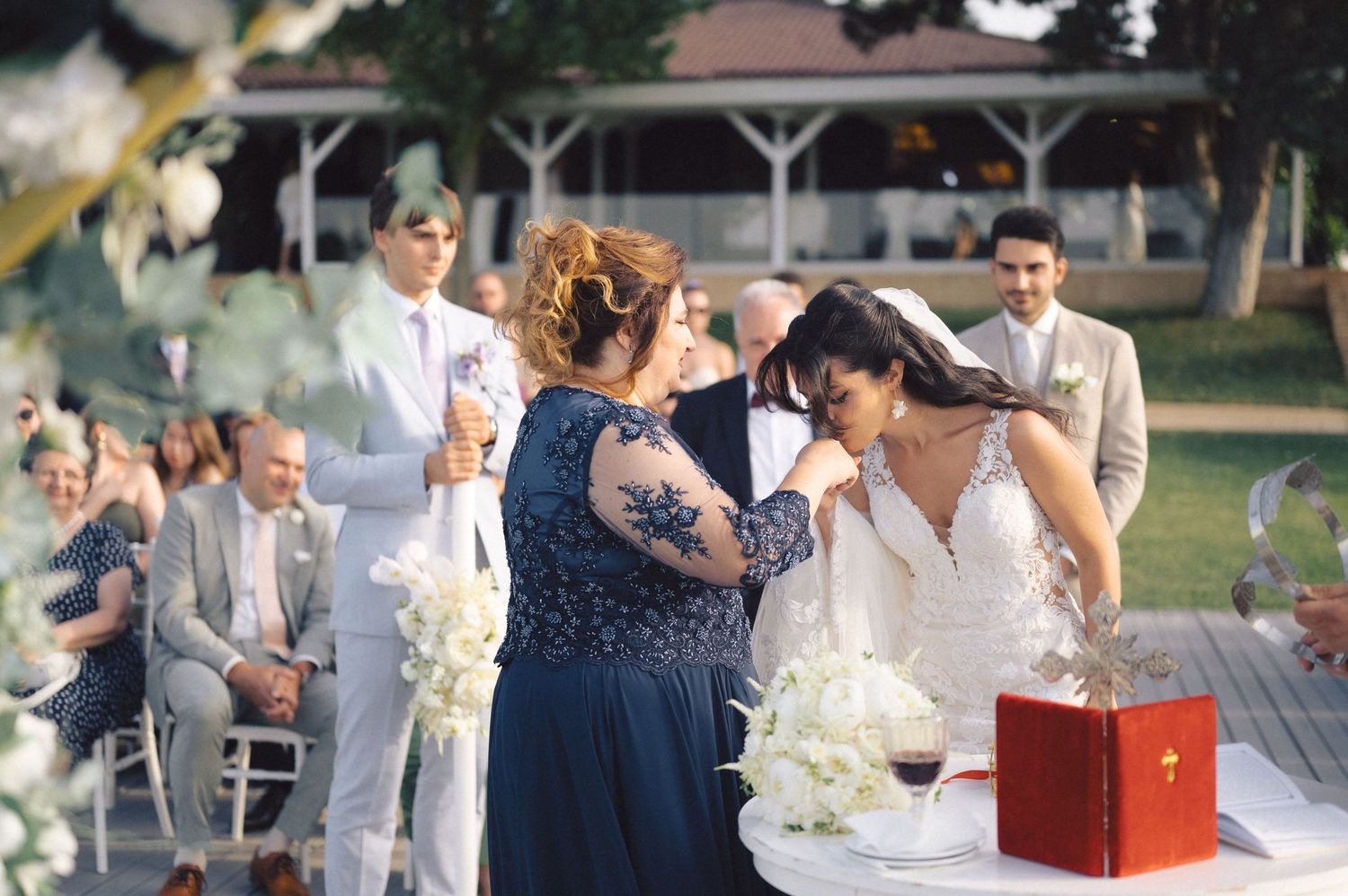 A celebratory wedding ceremony takes place outdoors with guests seated in white chairs and a decorated table setup.