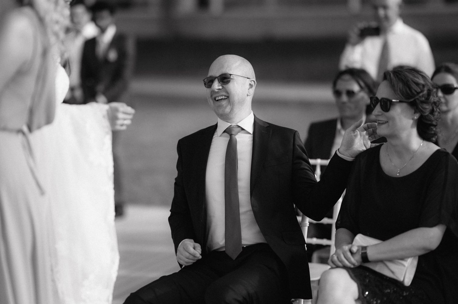 A candid black and white photo shows attendees smiling and conversing at a formal indoor gathering.