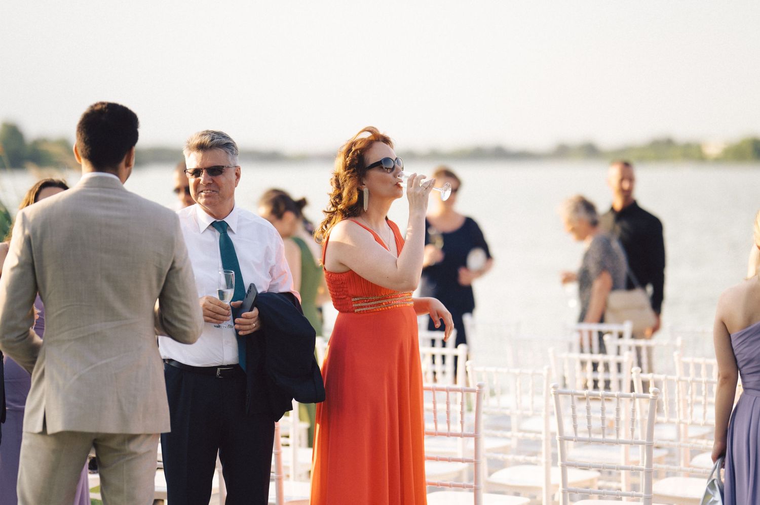 Wedding guests mingling during an outdoor reception with white chiavari chairs on a sunny day.