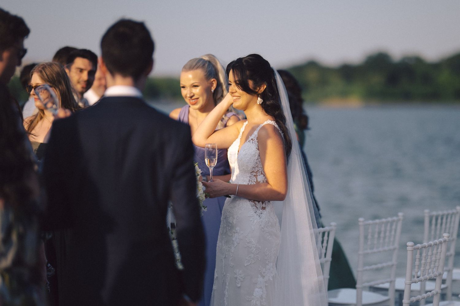 Romantic wedding reception by a scenic lakeside with elegant white chairs and floral decorations at sunset.
