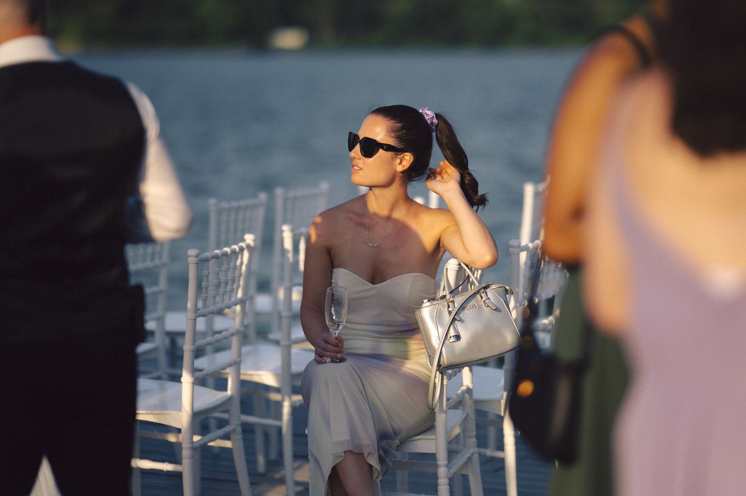 Wedding guests dining outdoors at elegant tables with glass place settings and soft pink decor under evening lighting.