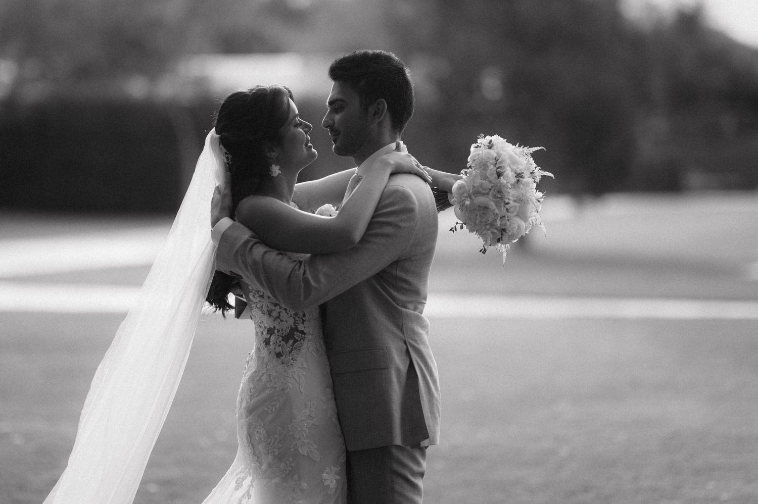 A romantic black and white portrait captures a couple embracing on their wedding day with bride holding bouquet.