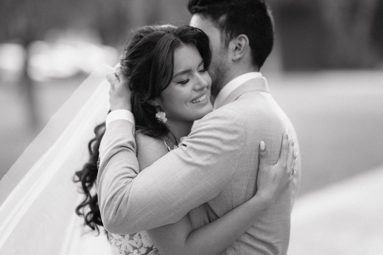 Black and white wedding photo showing couple embracing in romantic moment with bride wearing long veil.