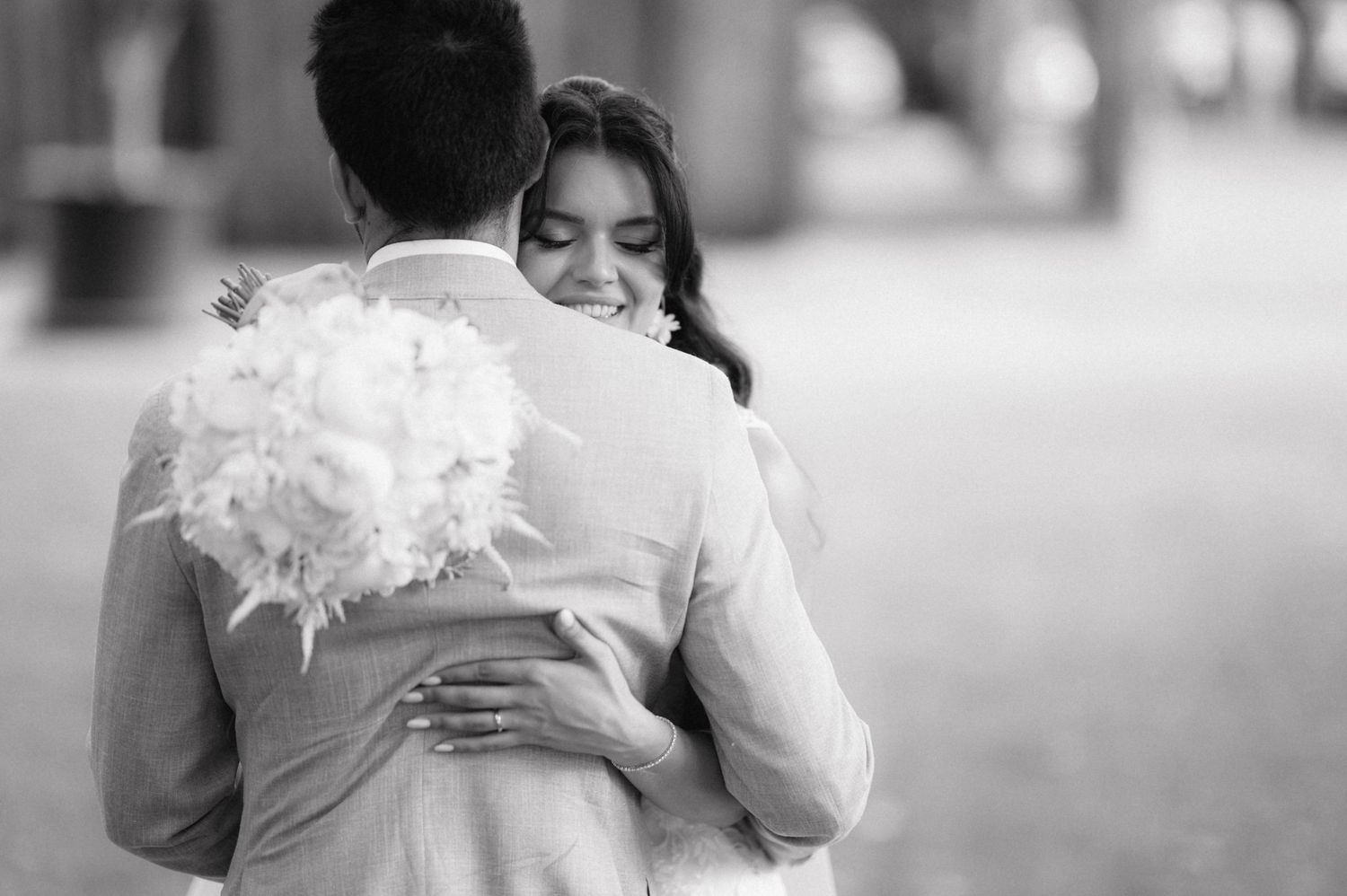 A tender black and white wedding moment shows an embrace while holding a white feathered bouquet.
