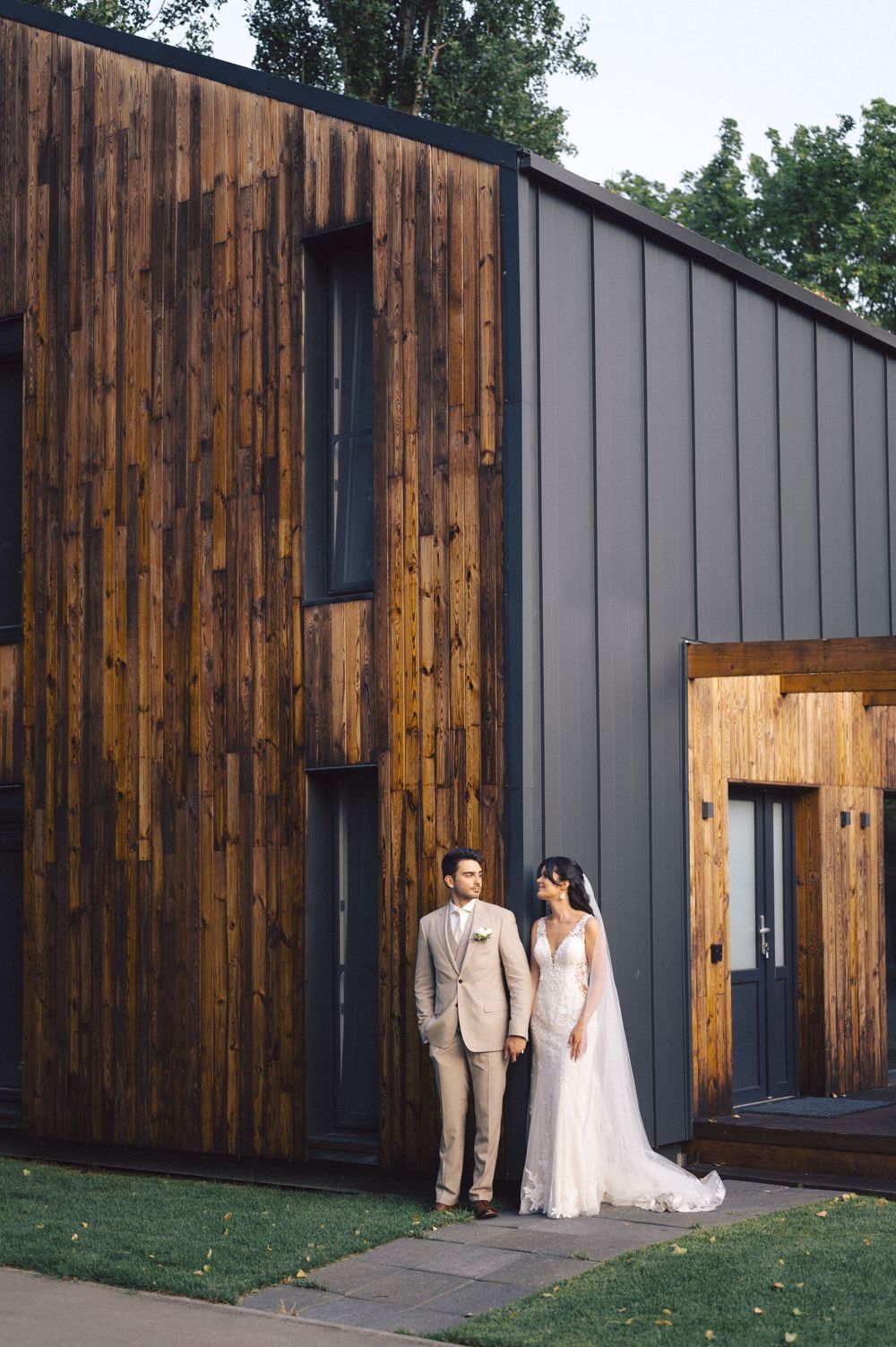 Modern wedding venue featuring rustic wood paneling and metal siding with a couple standing against the contemporary architecture.