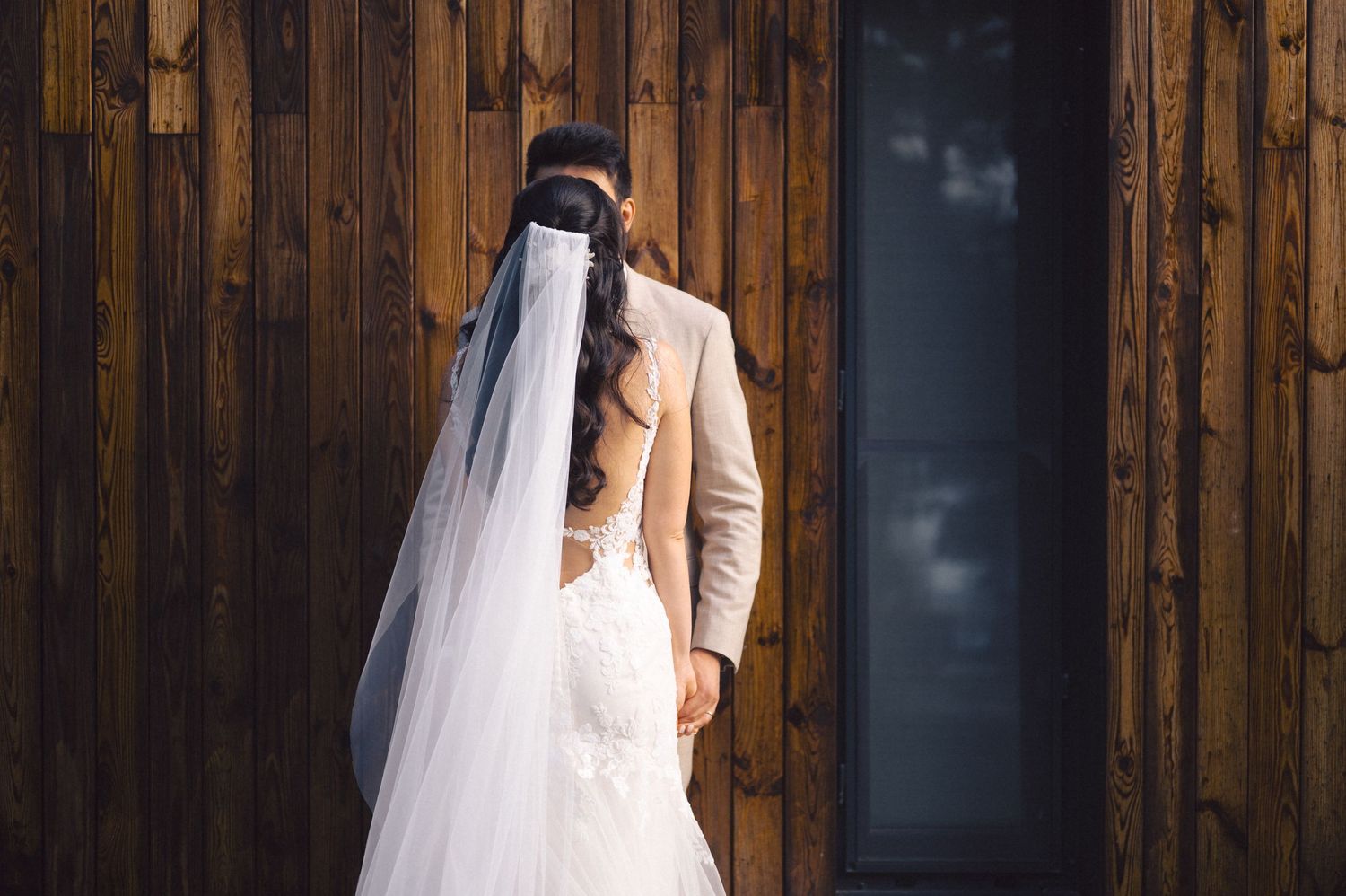 Romantic wedding portrait in front of wooden paneling features bride in flowing white gown and veil.
