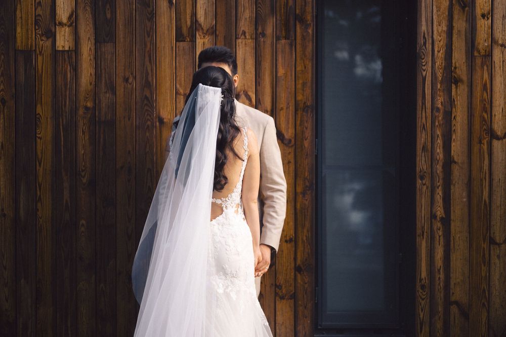 Romantic wedding portrait in front of wooden paneling features bride in flowing white gown and veil.