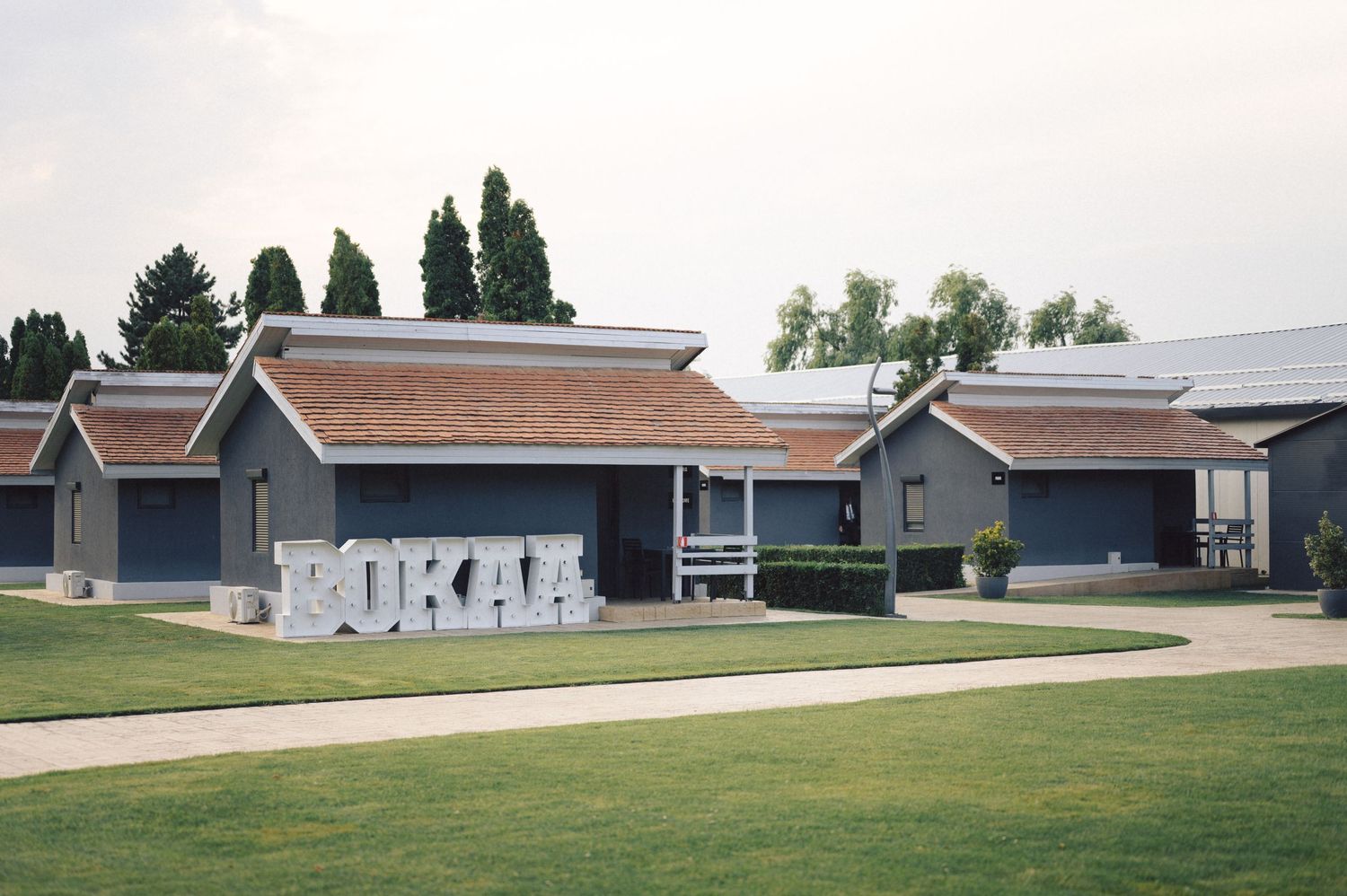 Row of modern gray buildings with brown roofs and grassy lawn in front on an overcast day.