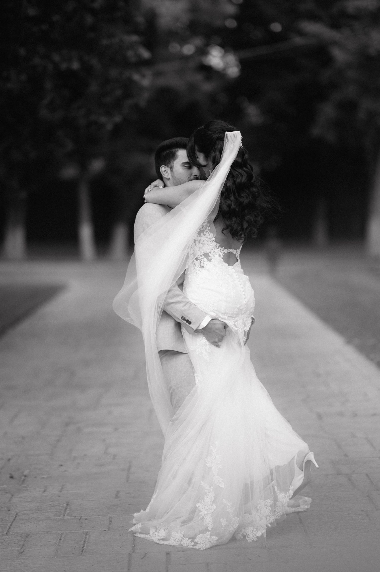 A romantic black and white photo of newlyweds dancing together outdoors, with the bride's dress flowing elegantly.