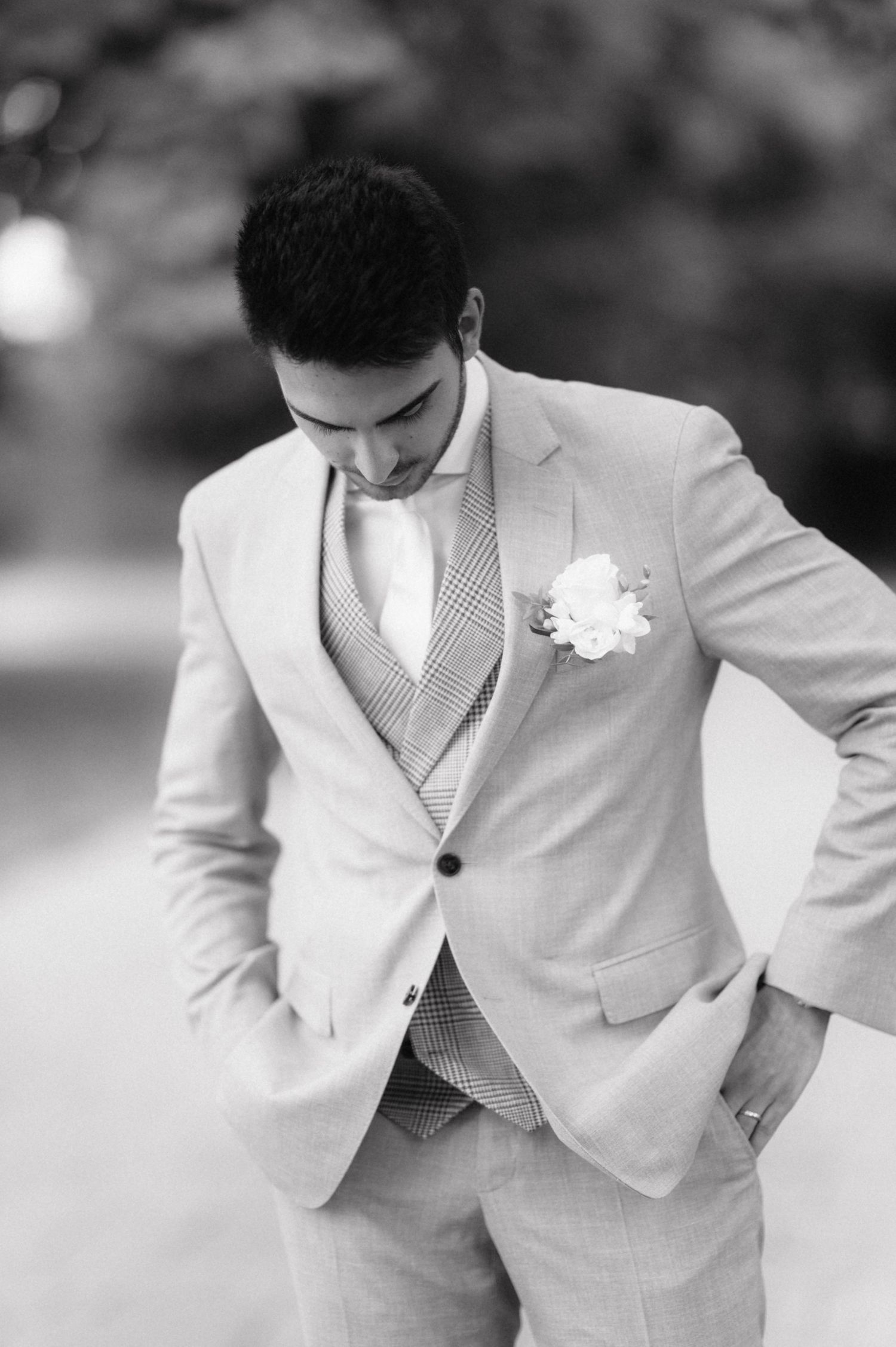 A groom in a light colored suit and vest adjusts his jacket while wearing a white floral boutonniere.