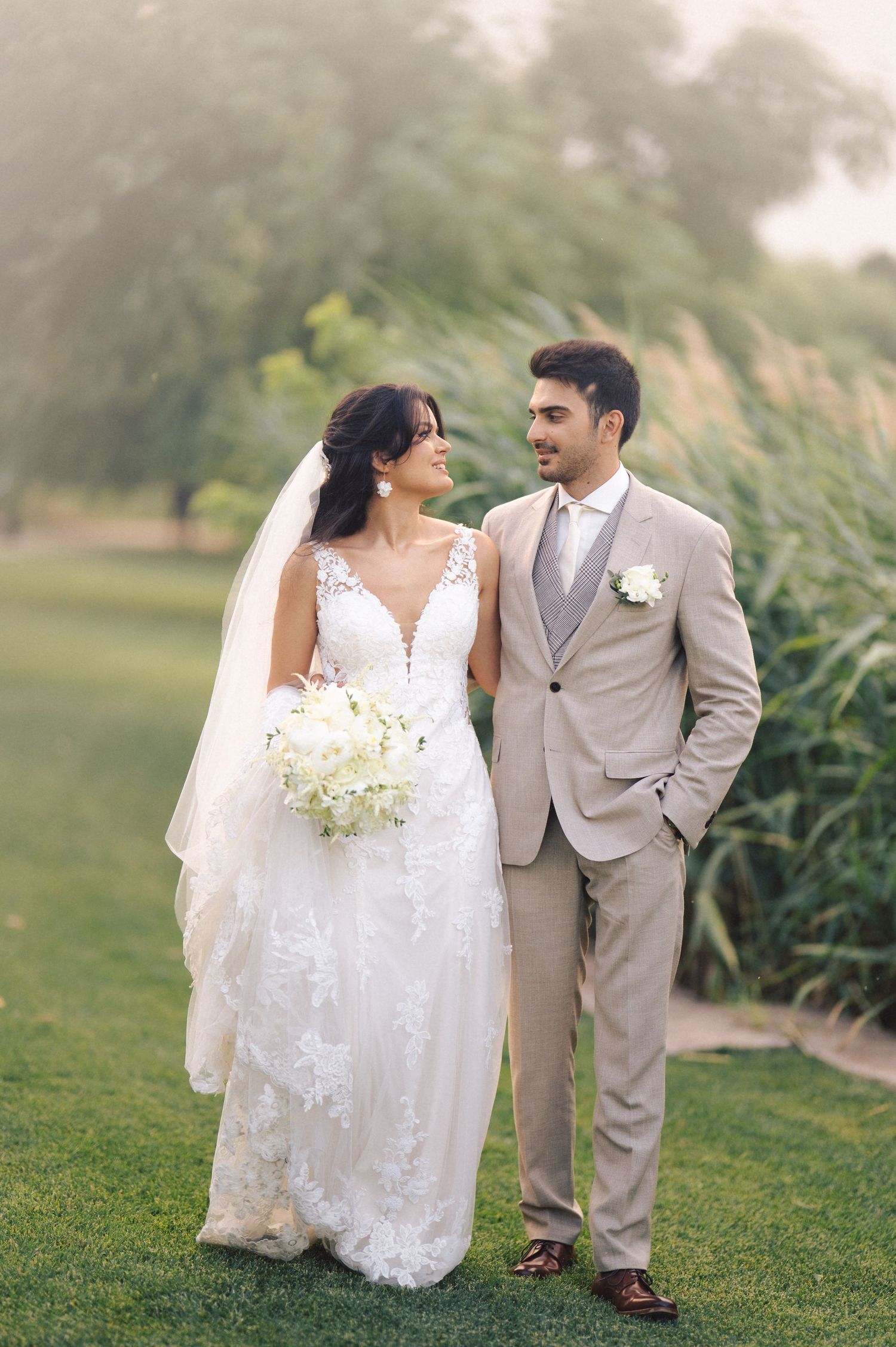 A bride and groom share romantic moments on their wedding day while walking through lush green grounds in outdoor photos.