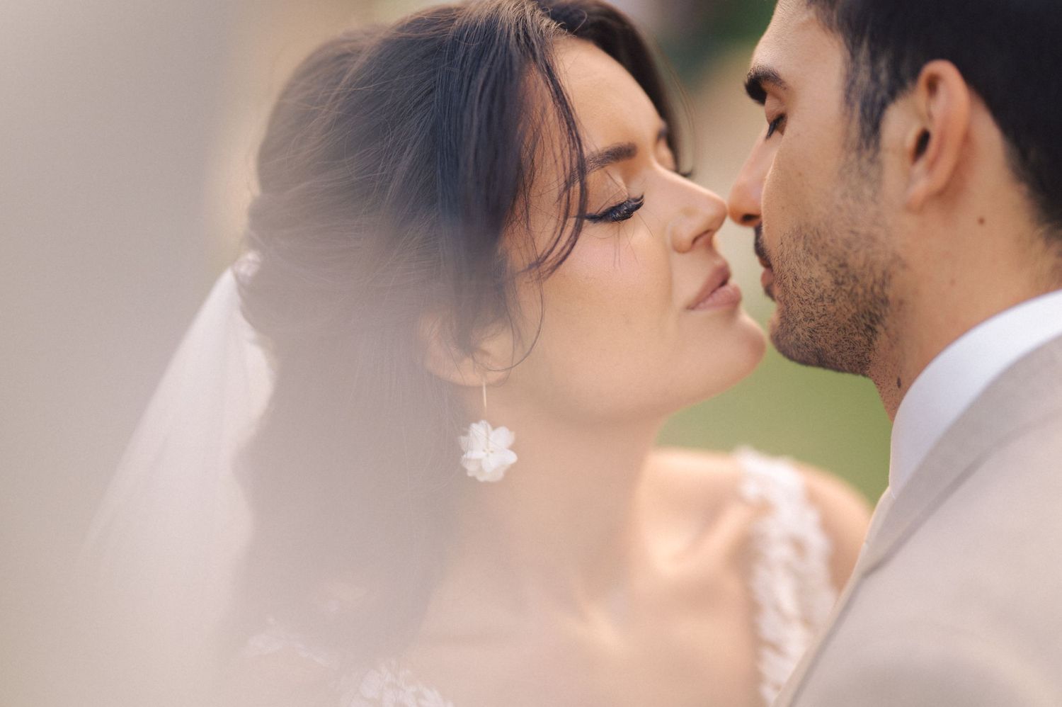 A romantic wedding moment captured through soft focus with the couple sharing a tender kiss under a delicate veil.