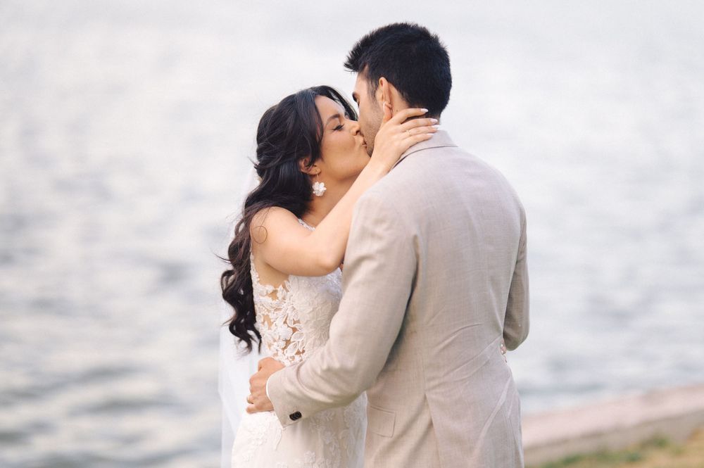 A romantic seaside wedding kiss moment with the couple embracing against a soft misty backdrop by the water.