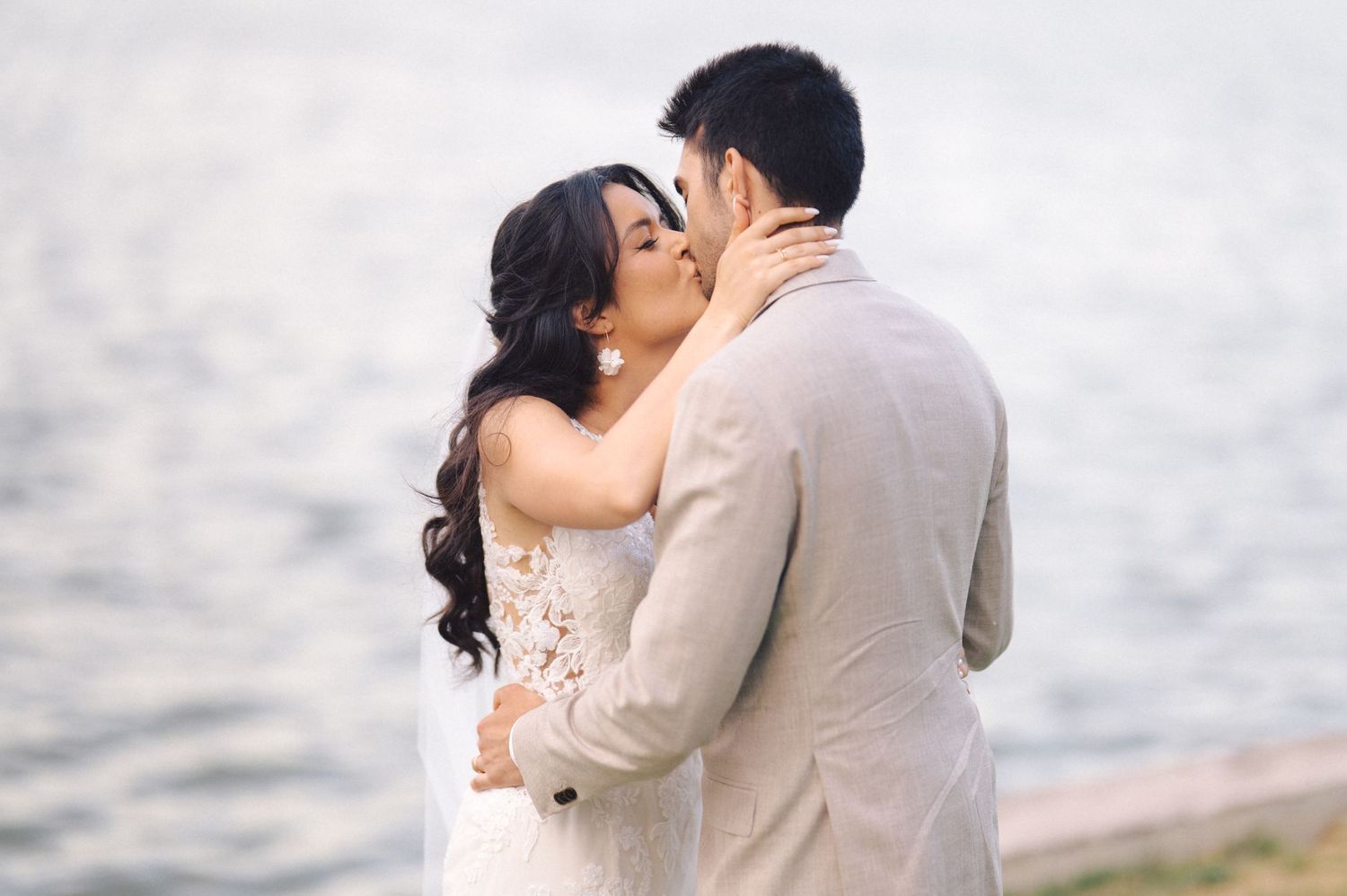 A romantic seaside wedding kiss moment with the couple embracing against a soft misty backdrop by the water.