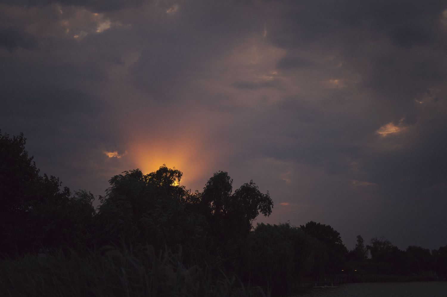 Silhouette of trees against a dramatic sunset sky with clouds in an orange and purple twilight.
