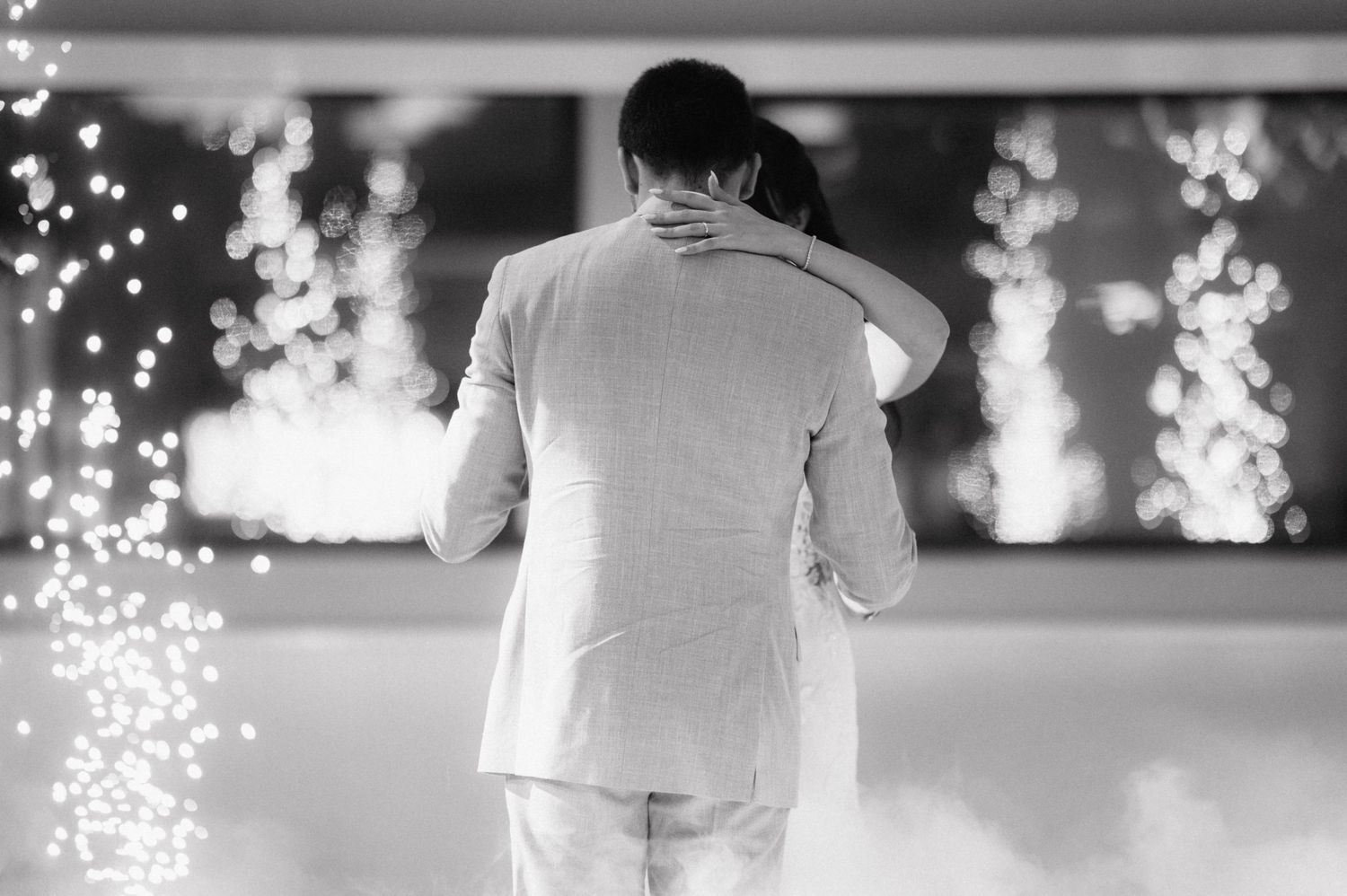 A black and white photo of a romantic slow dance at a wedding reception with twinkling lights in the background.
