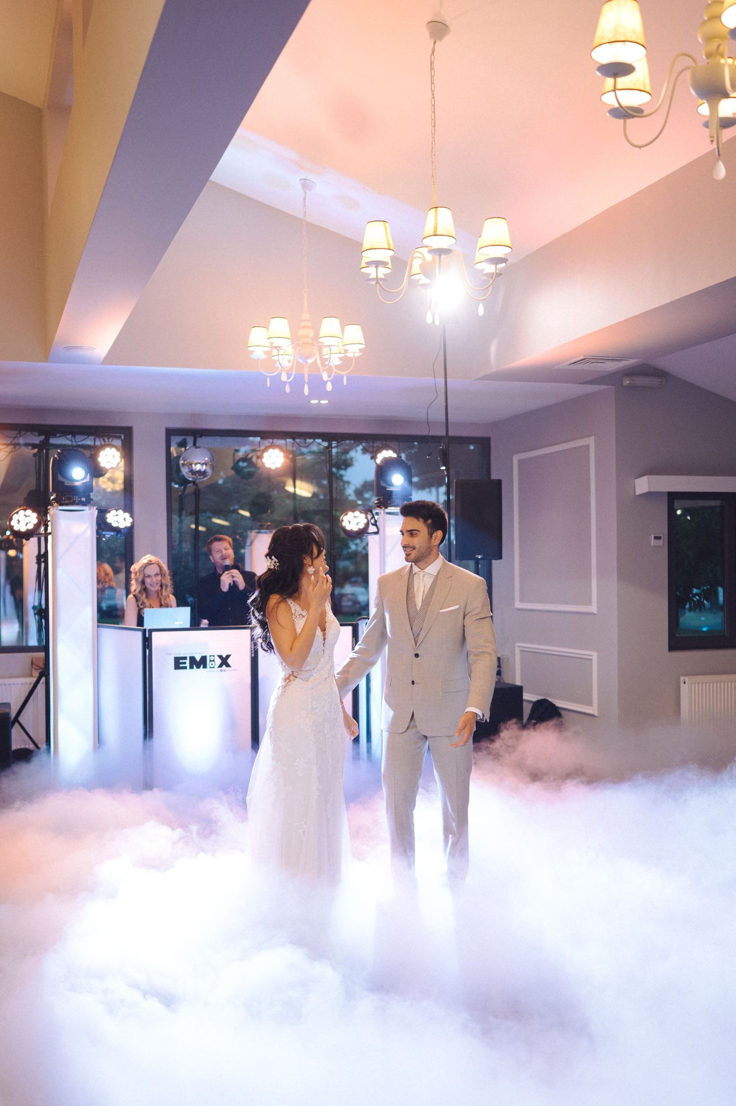 Wedding guests dance amid dramatic fog effects on an elegant dance floor with chandeliers overhead.