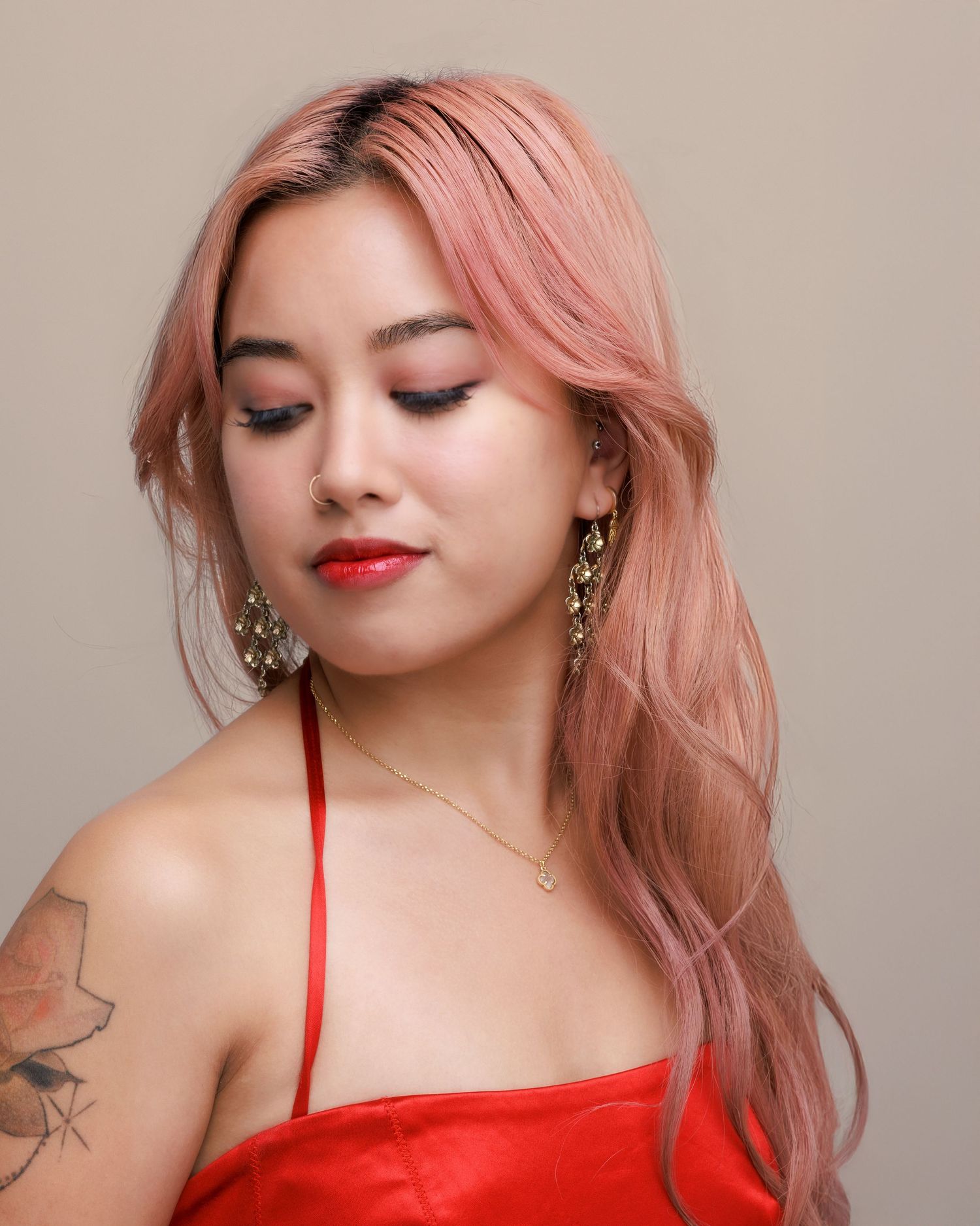 Portrait of person with pink hair wearing red top and statement earrings.
