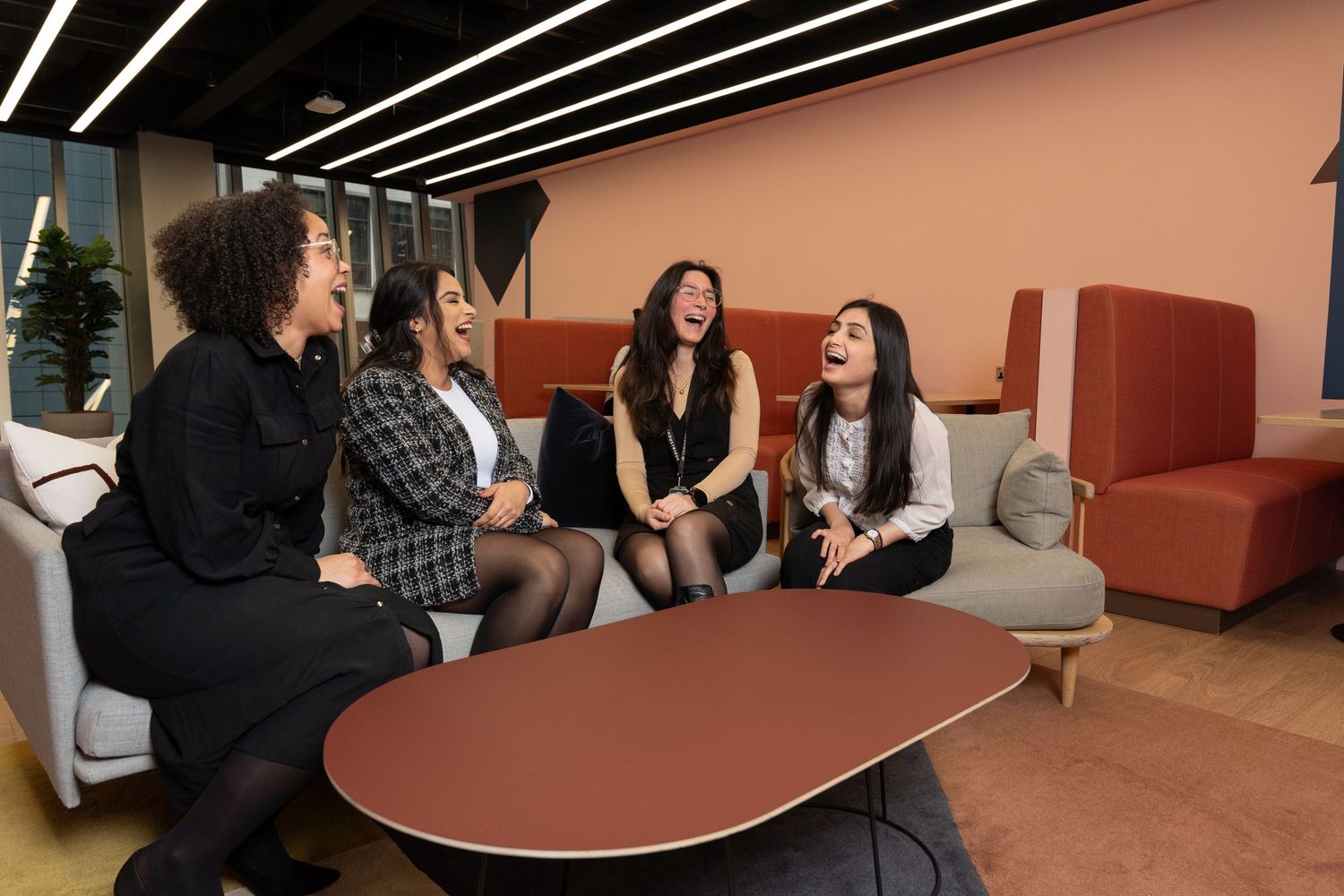 A group of female professional laugh and joke on a sofa in the break out area of their office St Mary Aex in The City, Central London