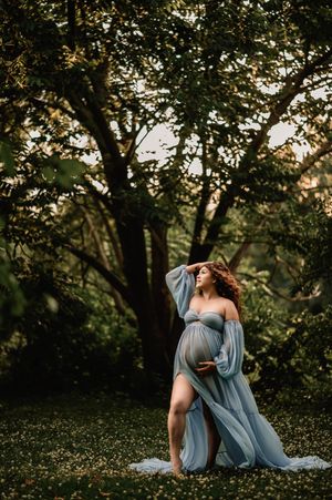 Romantic couple in a blue gown embrace during golden hour photoshoot in a lush garden setting.