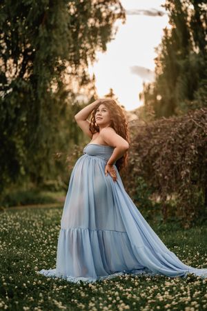 A person in a flowing light blue dress poses gracefully in a meadow of daisies during golden hour sunset.