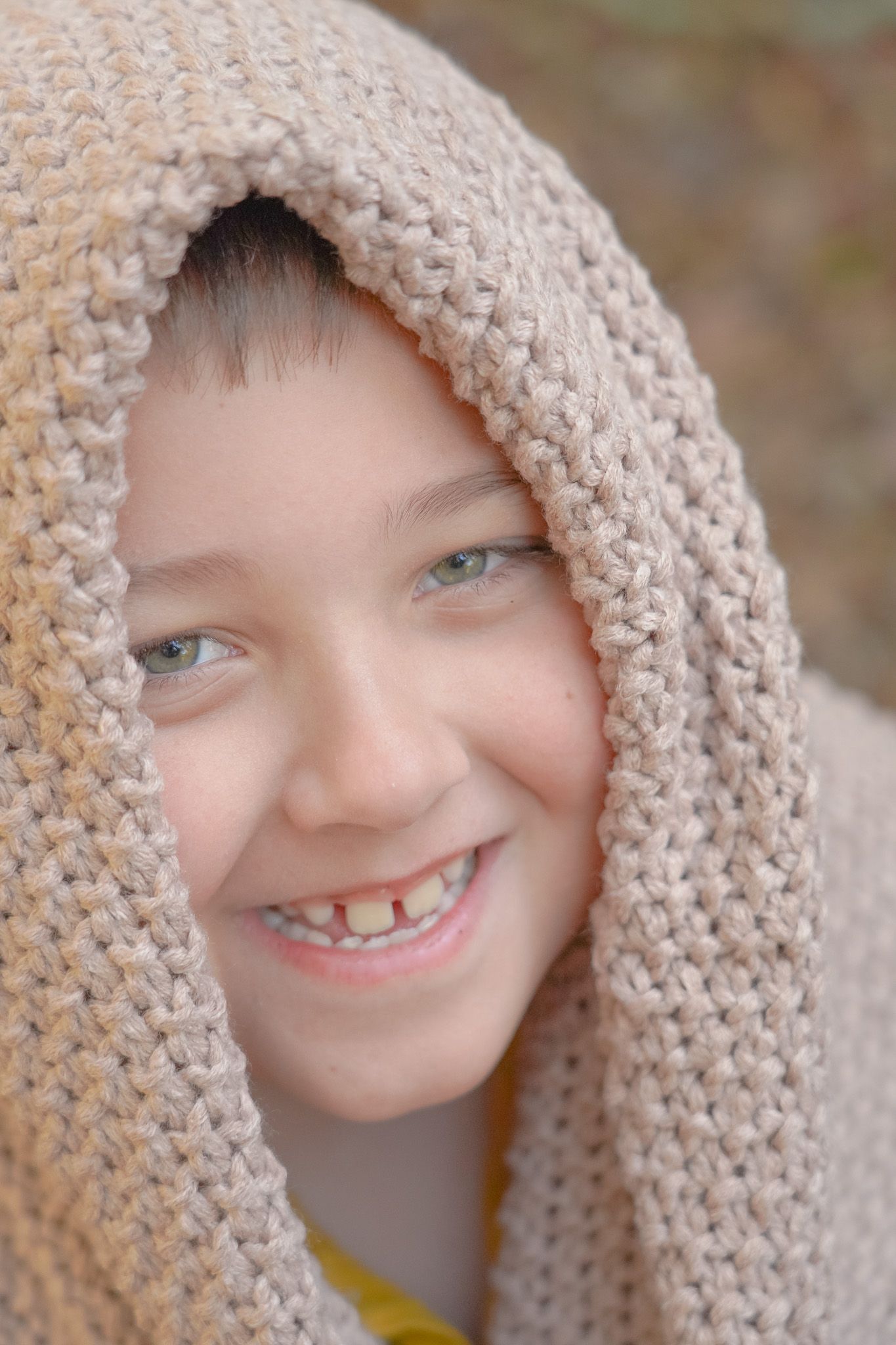 A cheerful smile peeks out from beneath a cozy beige knit blanket in a soft, warm portrait. Lincolnton NC Family Photography