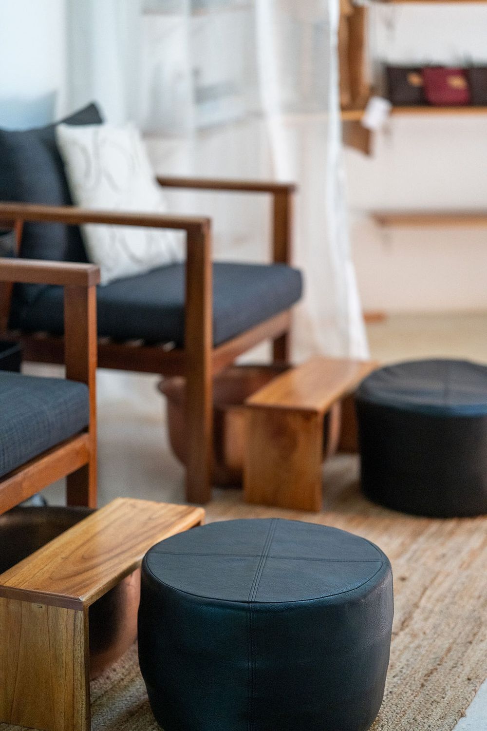 Modern spa waiting area with wooden furniture and black leather poufs on hardwood flooring.