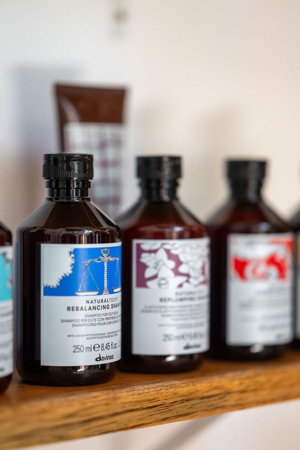 A row of brown glass bottles containing hair products sits on a wooden shelf with varying label designs.