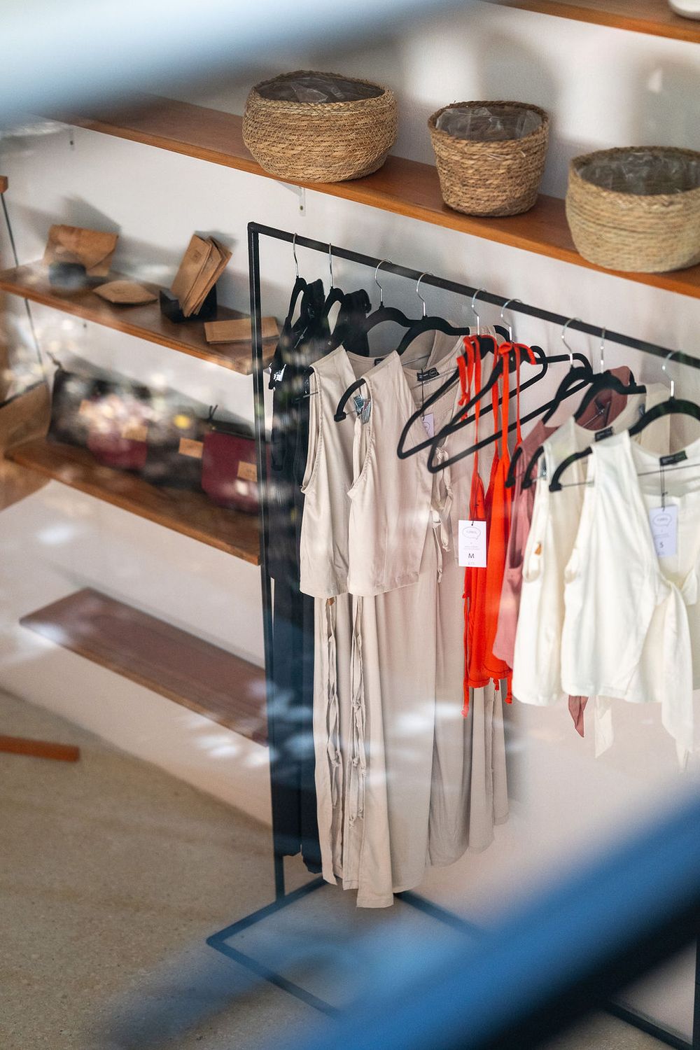 Organized retail display with woven baskets on shelves and clothing rack featuring white and red garments.