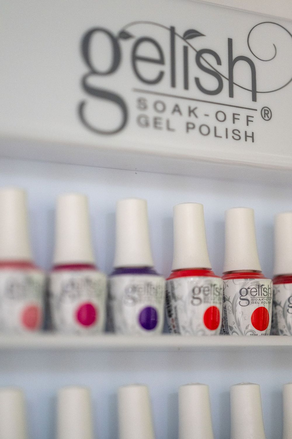 Display of colorful Gelish soak-off gel polish bottles arranged on white shelves showing brand logo and product lineup.
