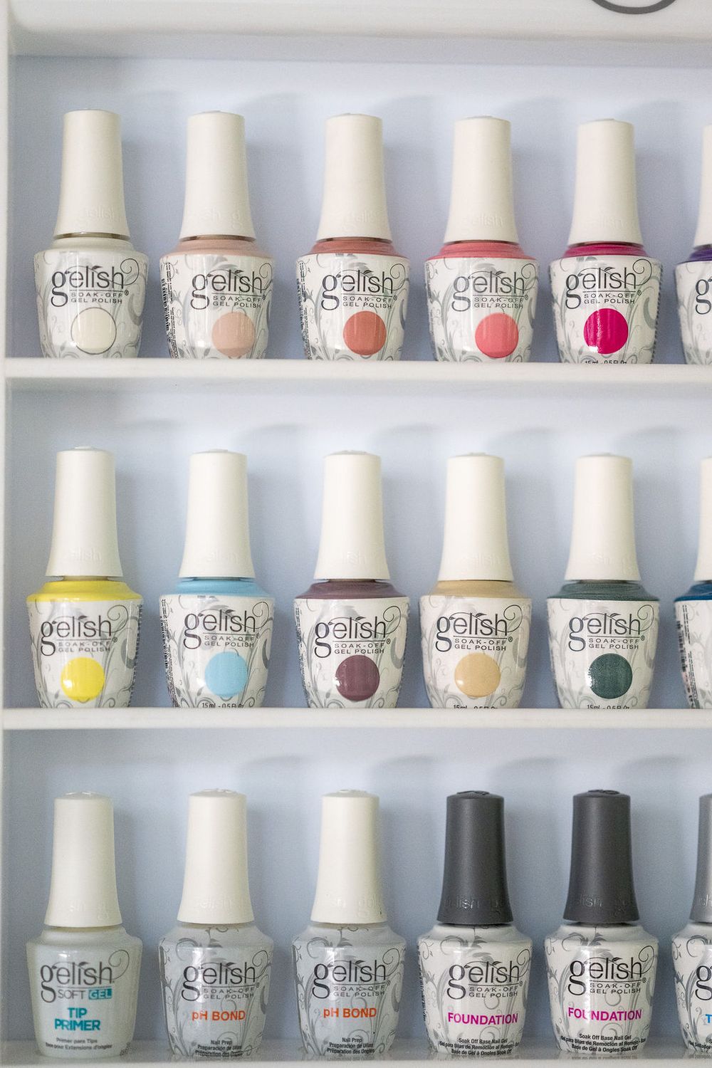 Rows of white nail polish bottles neatly arranged on white shelves displaying Gelish brand products in a salon setting.