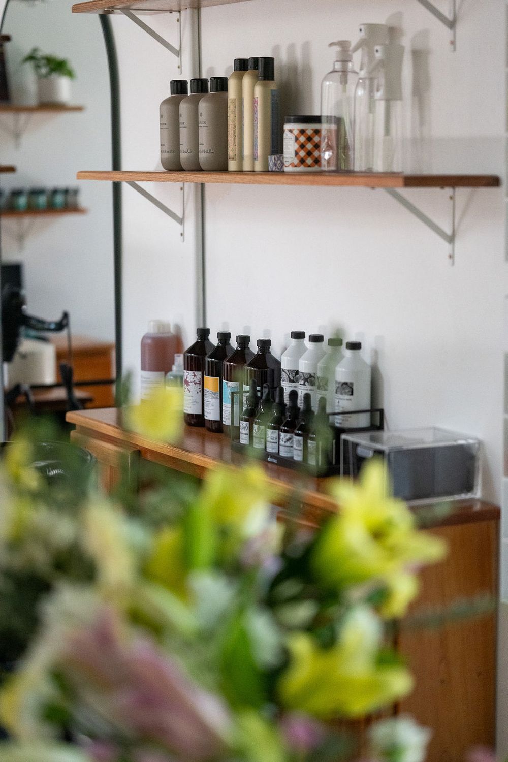 Wooden shelves displaying various hair salon products and bottles with soft focus flowers in the foreground.