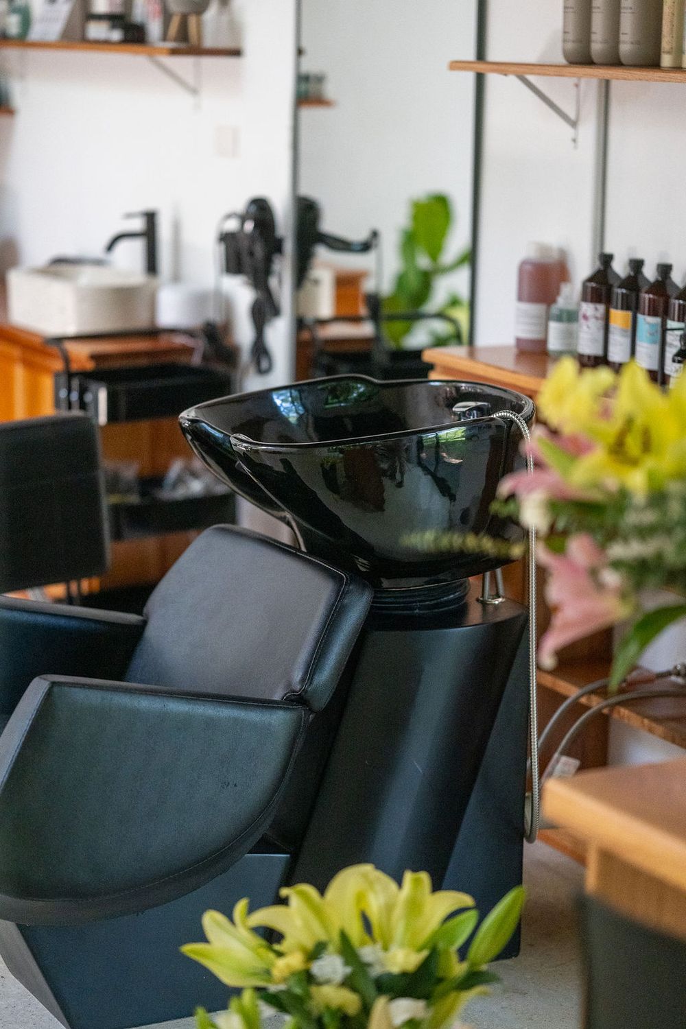 Modern black shampoo bowl and reclining chair in a sleek salon interior with green plant decor visible.