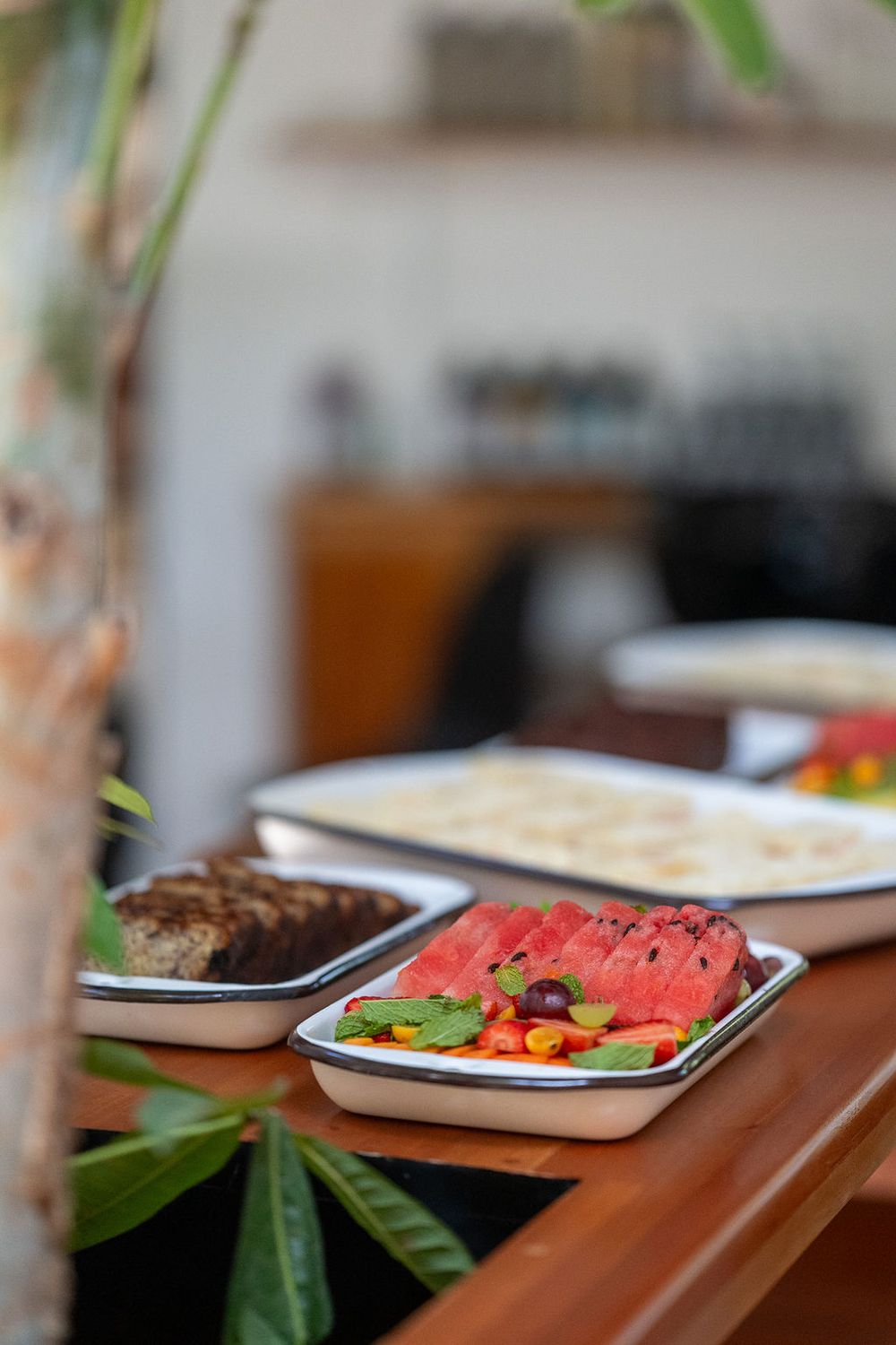 Fresh watermelon slices and other snacks arranged on white plates sitting on wooden table surface.