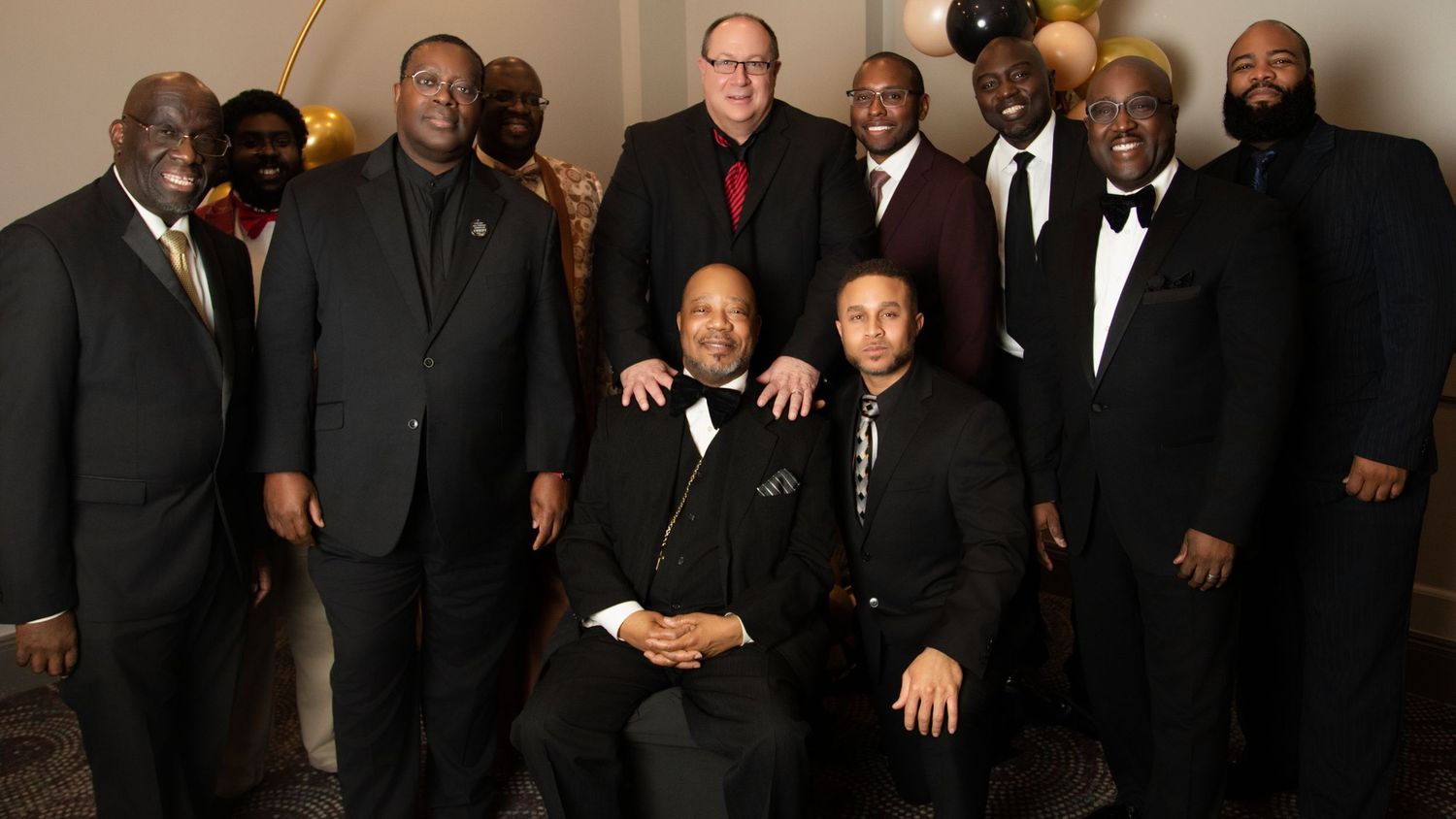 Large group wearing formal black attire posed for panoramic photo.