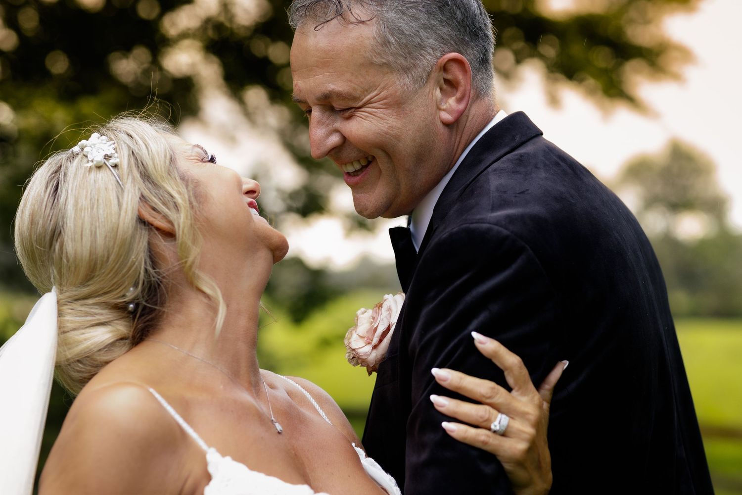 A couple laughs joyfully during an outdoor wedding photoshoot against a green lawn during golden hour.