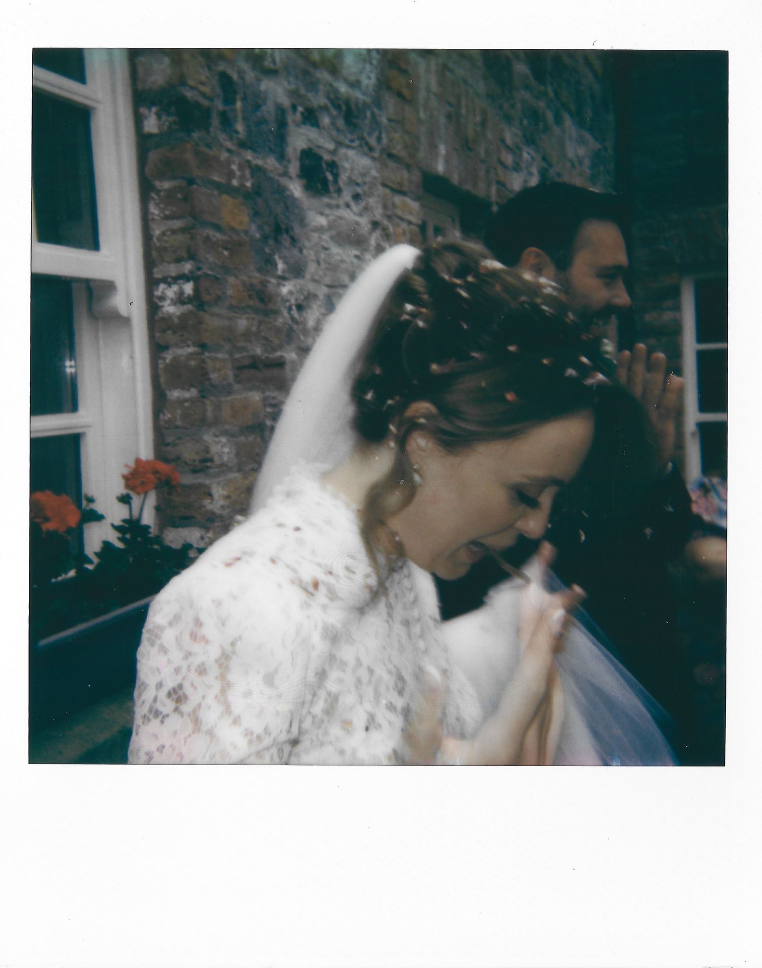 A figure in a white lace dress is photographed in vintage-style lighting against a stone wall backdrop.