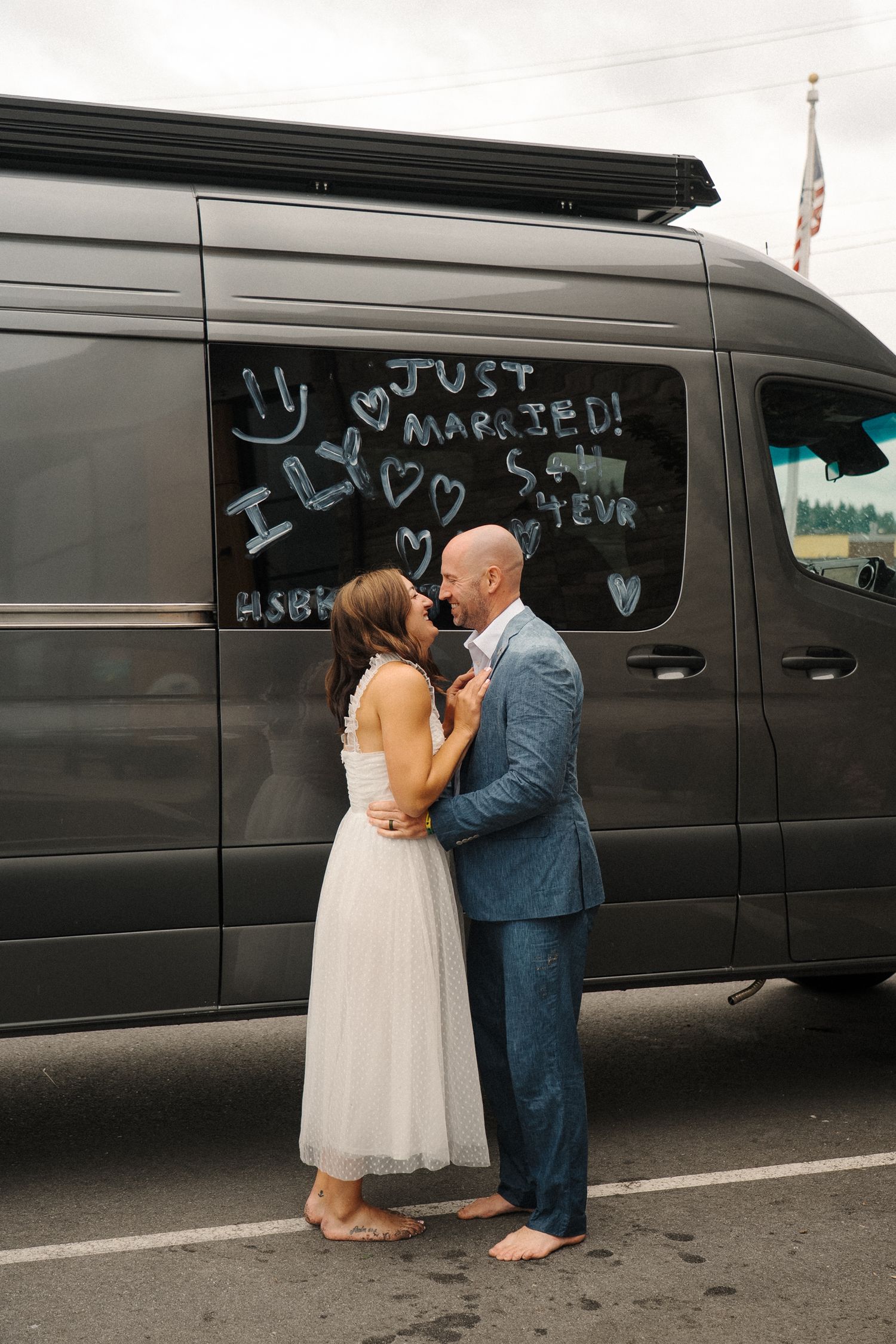 A couple shares a romantic moment next to a van with a 'Just Married' message written on its side panel.
