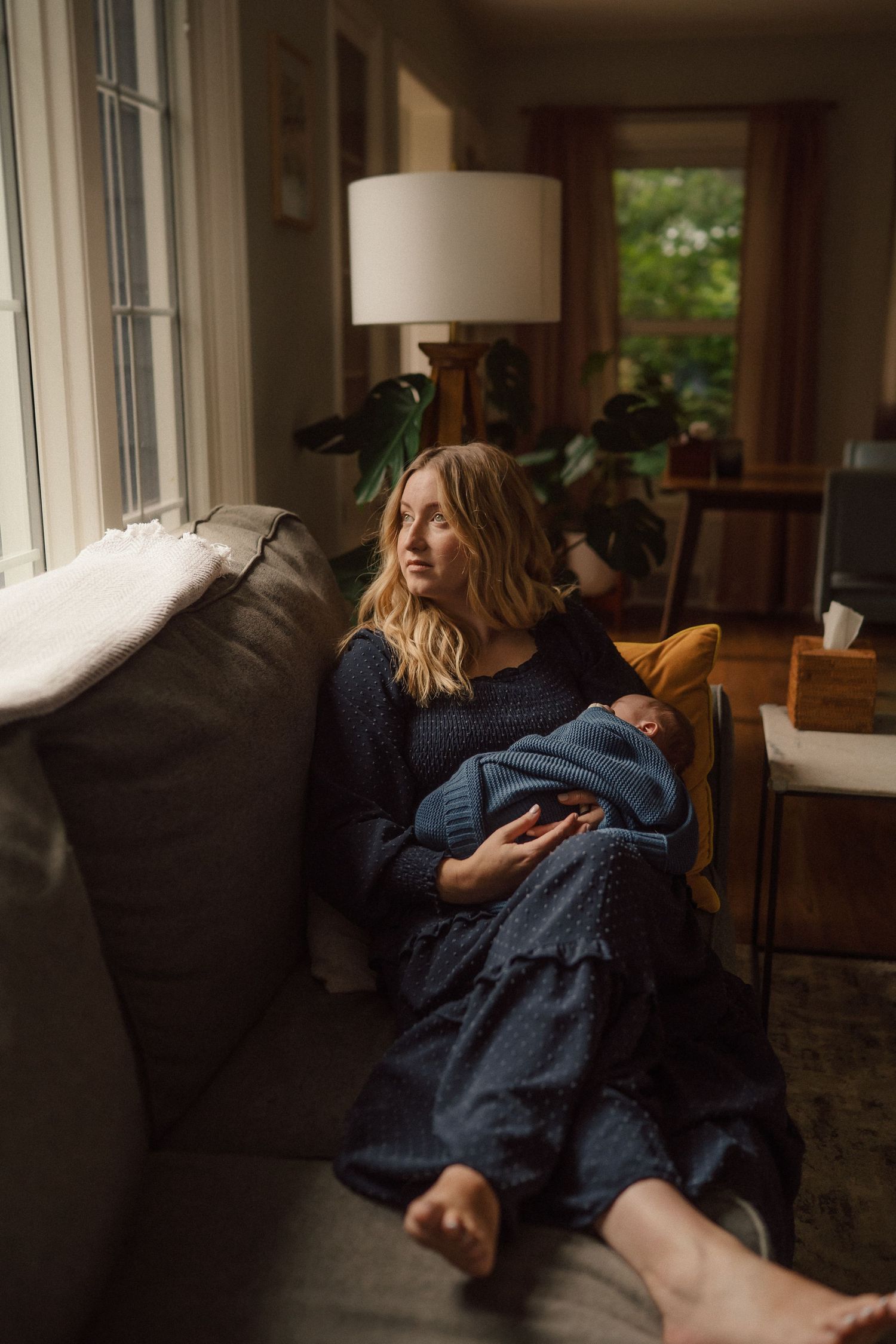 Intimate moments captured in natural light on a navy couch near sunlit windows.