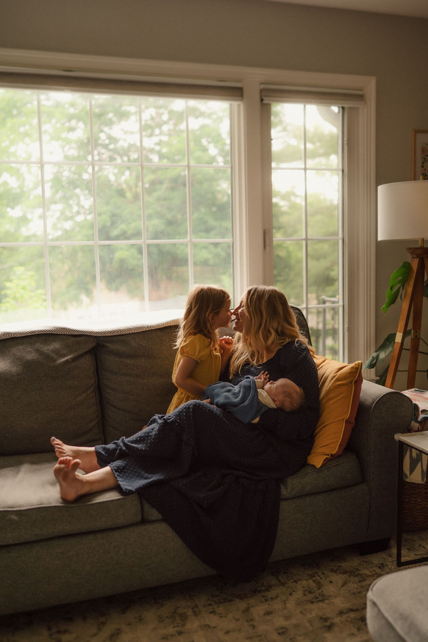 A cozy living room scene with family members relaxing on a grey couch by large windows with natural light.