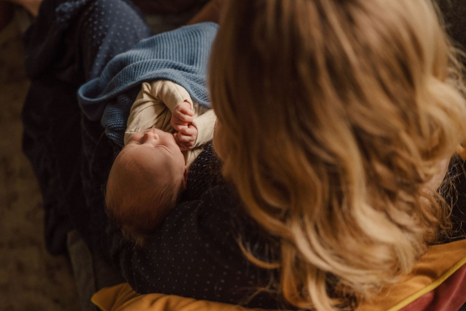 A newborn wearing a blue knit hat rests peacefully indoors.