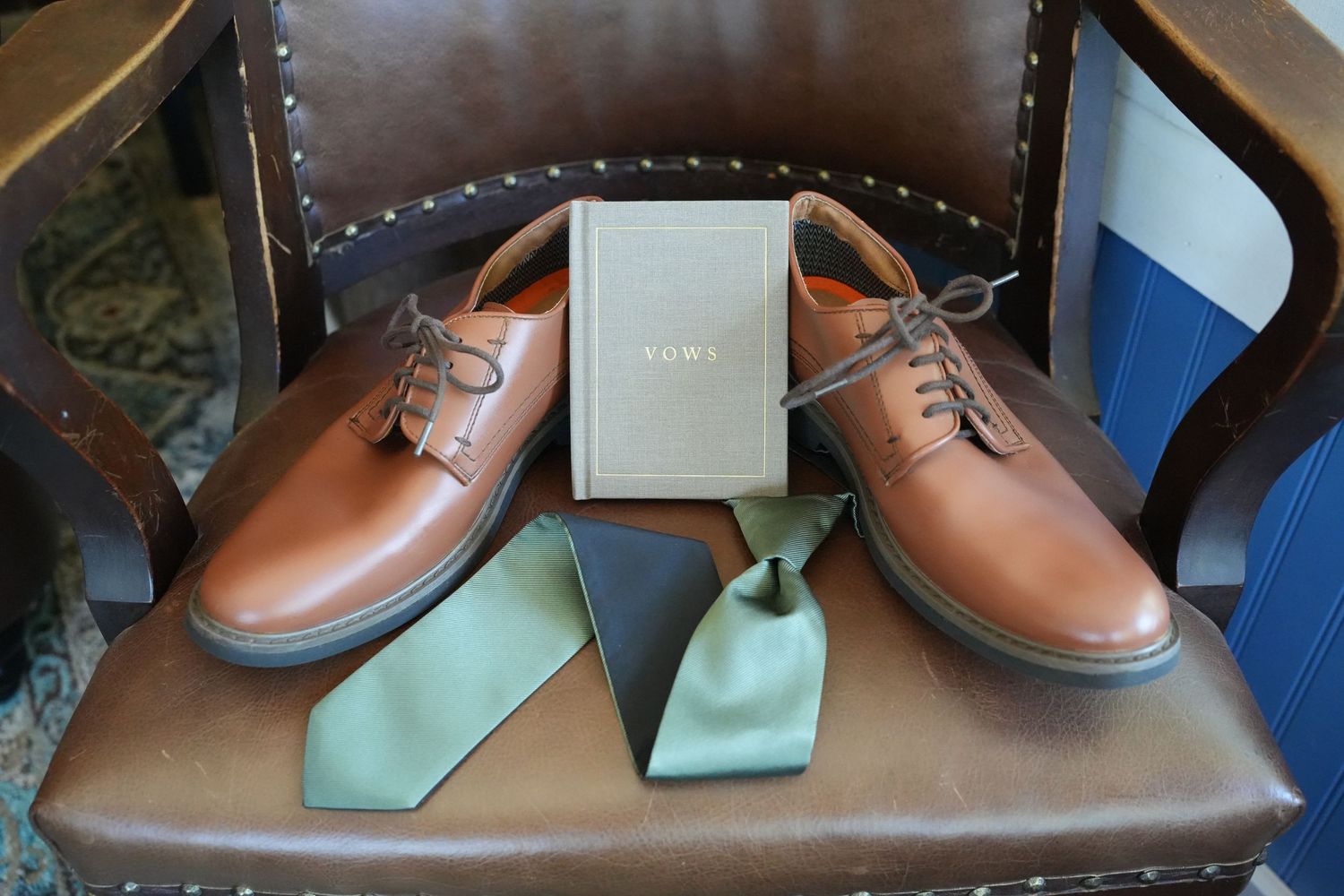 Grooms' details photo with shoes, vow book, and green tie