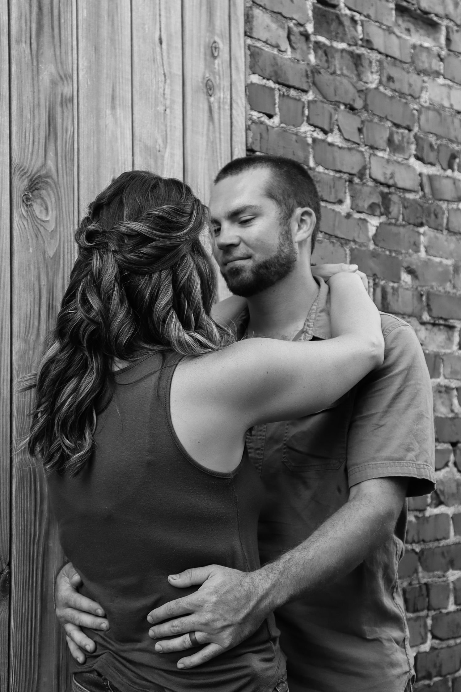 Black and white intimate couple photos against rustic brick and wooden wall backdrop.
