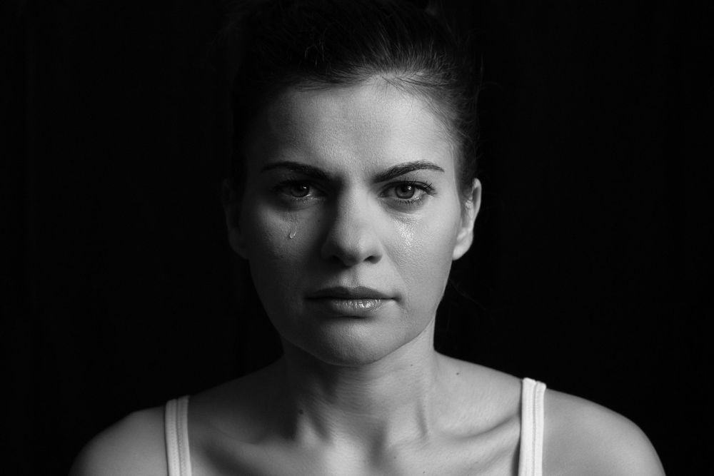 Black and white portrait of a person wearing a white tank top with a dramatic lighting against a dark background.