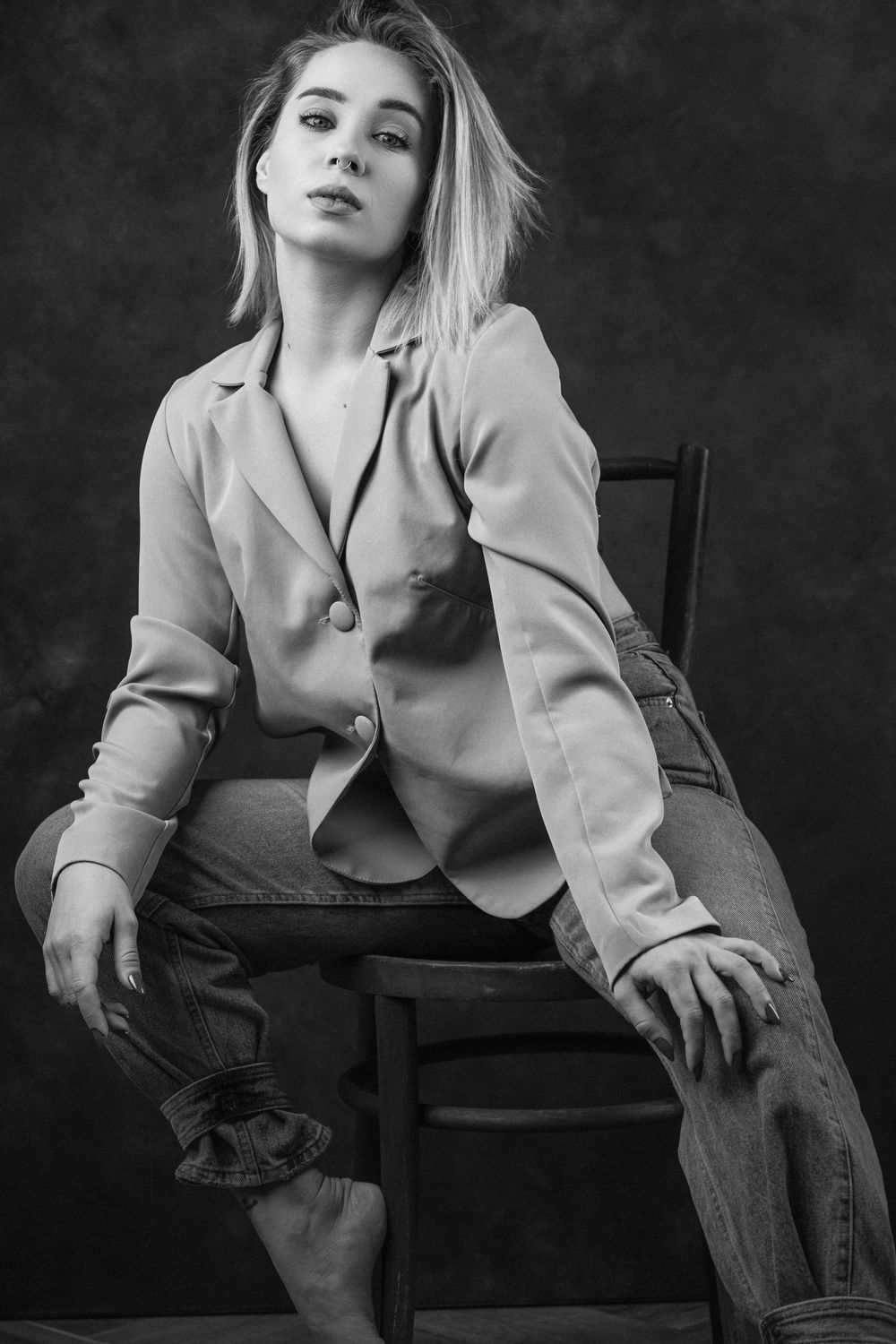 A dramatic black and white photo series showing someone in a light blazer posing artistically on a dark chair.